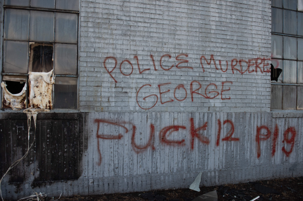 Ein Gebäude mit Graffiti, das "Polizei Mord George Fuck 12 P19" auf der Seite trägt, mit Fenstern und diversen Gegenständen vorne drauf.