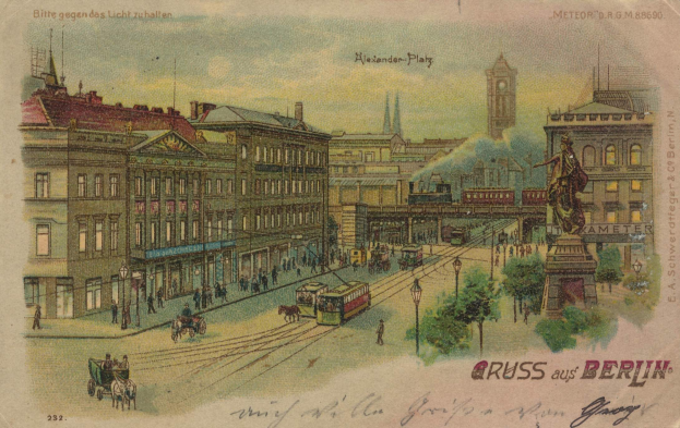 Schwarz-Weiß-Postkarte einer belebten Berliner Stadtstraße mit Gebäuden, Straßenlaternen, Fahrzeugen, Pferdefuhrwerken, Fußgängern, Bäumen, einer Statue und einem bewölkten Himmel.