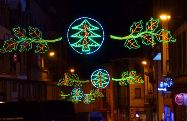Eine Stadtstraße mit festlichen Weihnachtslichtern in Form von Blättern geschmückt, mit Fahrzeugen, die die Straße entlangfahren, und Gebäuden auf beiden Seiten.