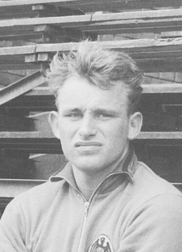 Schwarzes und weißes Foto eines Mannes in einer Jacke, der vor gestapelten Holzplanken steht, der angeblich ein legendärer deutscher Fußballspieler war, der im Alter von 89 Jahren starb.