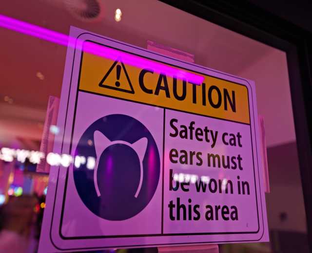 Hellgelbes Warnschild in einem Ladenschaufenster, das 'Sicherheitskatzenohren' trägt.