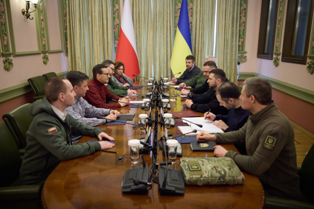 Eine Gruppe von Männern in einer offiziellen Umgebung mit Mikrofonen und Dokumenten an einem Holztisch, die eine Vereinbarung diskutieren, mit Flaggen und Lichtern im Hintergrund.
