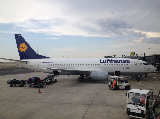 Lufthansa Airbus A320-200 am Frankfurter Flughafen auf dem Boden mit Flughafenfahrzeugen, Wagen, Verkehrskegeln, Beschilderung und einer bewölkten Himmel im Hintergrund.