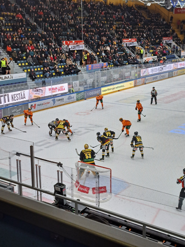 Gruppe von Menschen, die Hockey auf einem Eisstadion spielen, mit Zuschauern, Bannern und Flutlicht.
