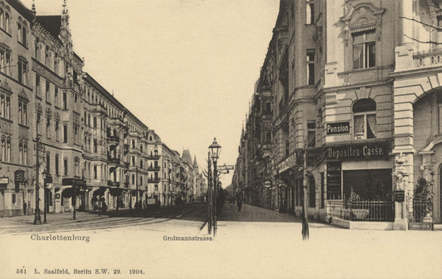 Altes Schwarz-Wei├č-Foto einer Stadtstra├če in Charlottenburg, Deutschland, mit Geb├Ąuden, Stra├čenlaternen, L├Ąmpchen, Schildern, Kraftfahrzeugen, Passanten, Gittern und einem klaren Himmel.
