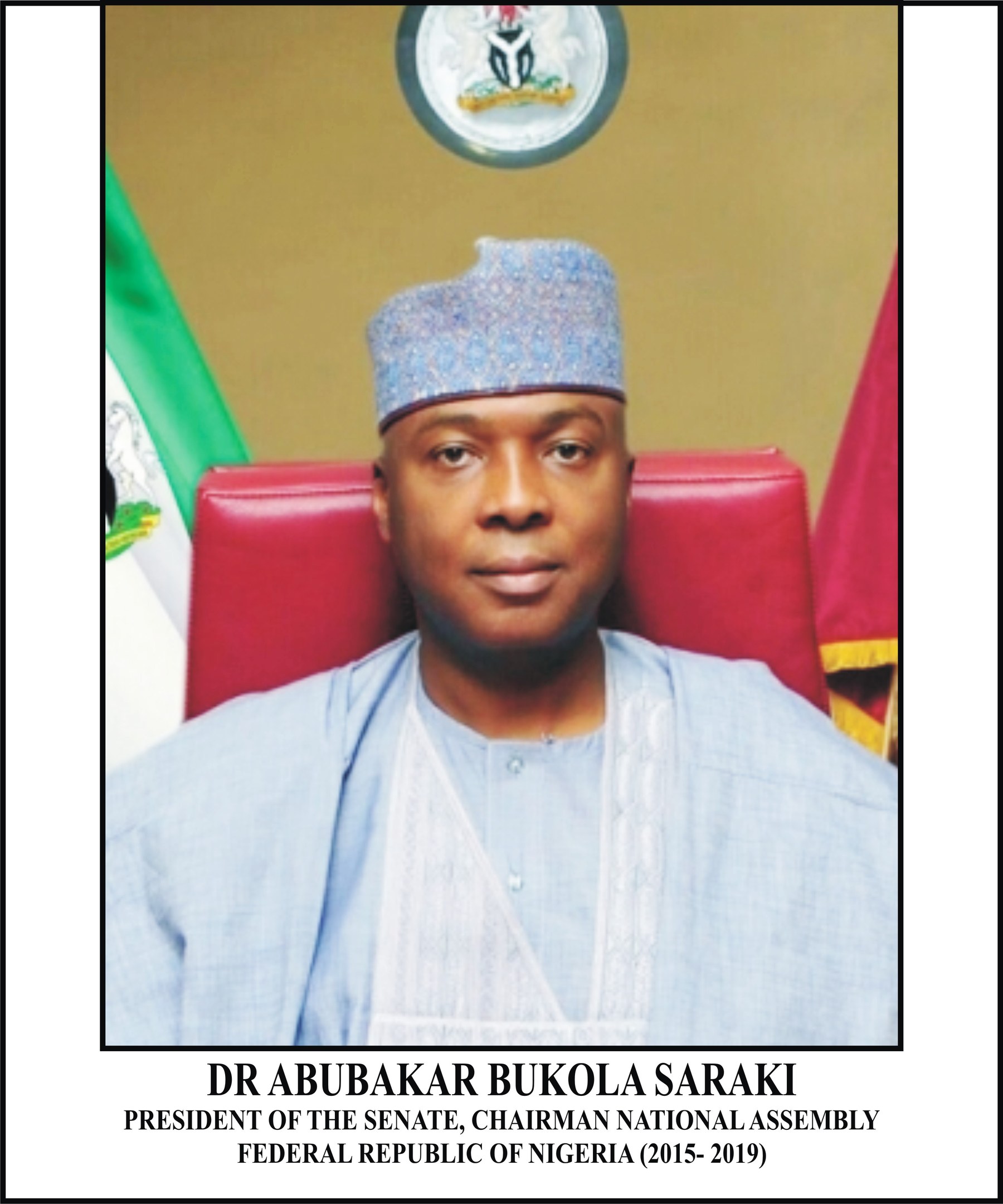 Dr. Abubakar Bukola Saraki, Präsident des Senats, sitzend in einem blauen Kleid und einer Mütze, mit zwei Flaggen und einer logogeschmückten Wand dahinter und einem Rahmen mit Namen unten.