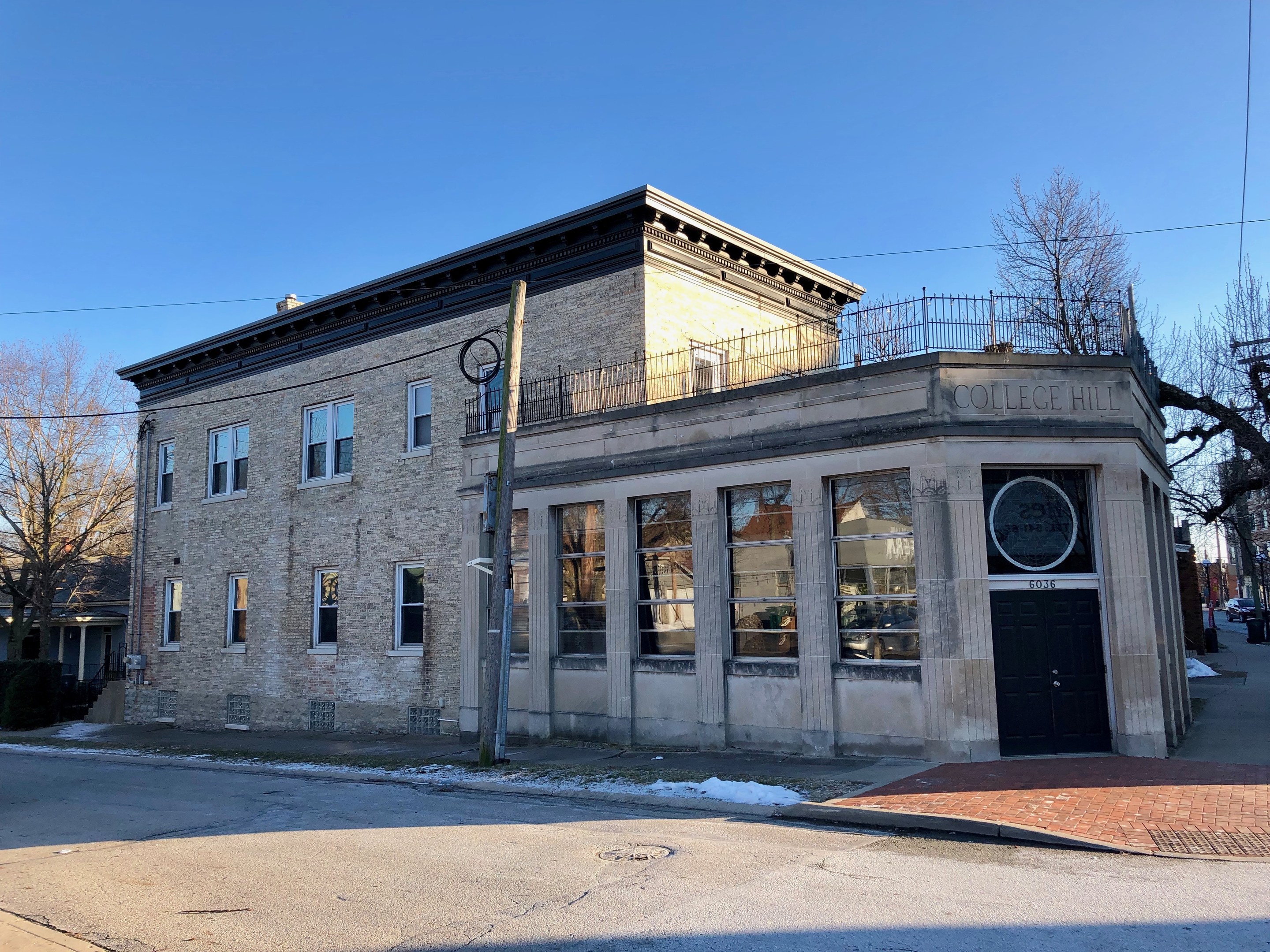 Außenansicht der College Hill Bibliothek, ein altes Gebäude an einer Straßenecke mit Fenstern, einer Tür, umgeben von Bäumen, Pfählen, Drähten und Fahrzeugen, unter einem Himmel als Hintergrund.
