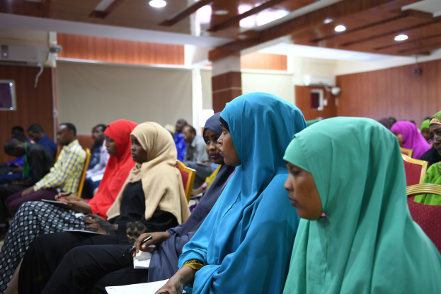 Eine Gruppe von Frauen sitzt in Stühlen in einem Raum, hält Bücher und Stifte und hat eine Wand, Deckenleuchten und eine Klimaanlage im Hintergrund, nimmt an einem Workshop zu Frauenrechten in Nigeria teil.