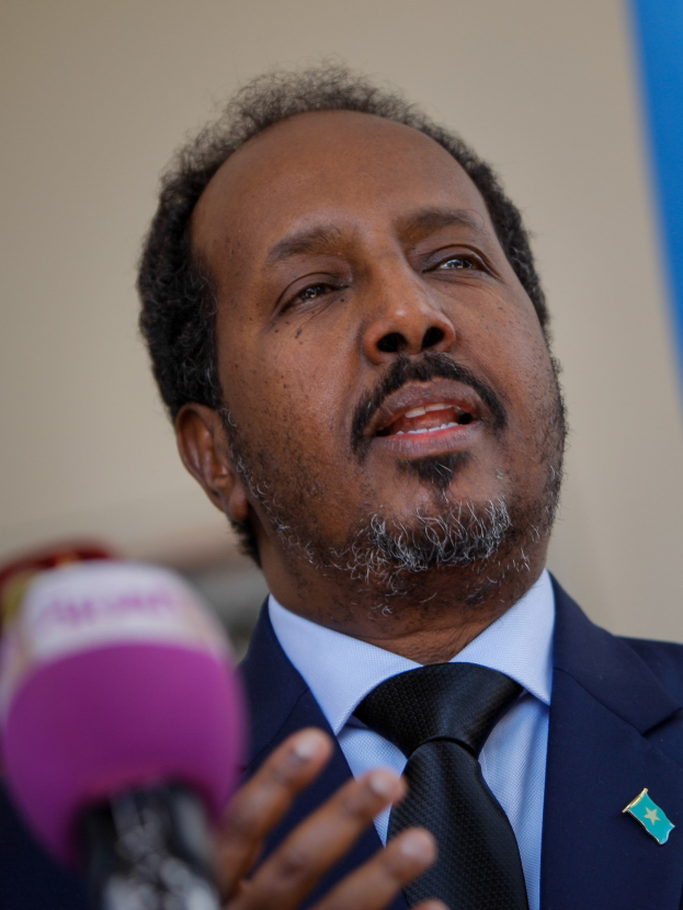 Ein Mann im Anzug und mit Krawatte spricht in ein Mikrofon an einem Podium, wahrscheinlich zu einem Publikum.