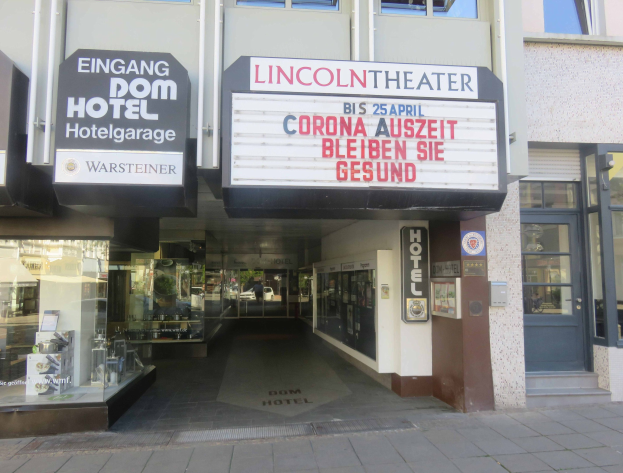Das Lincoln Theater in Berlin, Deutschland, mit Glasfenstern und -türen und einer Texttafel außen sowie einer belebten Stadtlandschaft, die durch den Eingang zu sehen ist.