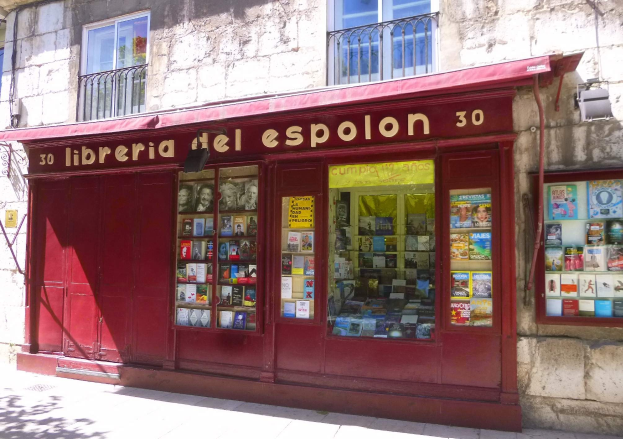 Ein zweistöckiges Gebäude mit einer Schaufensterfront, die ein rotes Vordach trägt, auf dem 'Libreria del Espolon' steht und ordentlich sortierte Bücher im Inneren zeigt.
