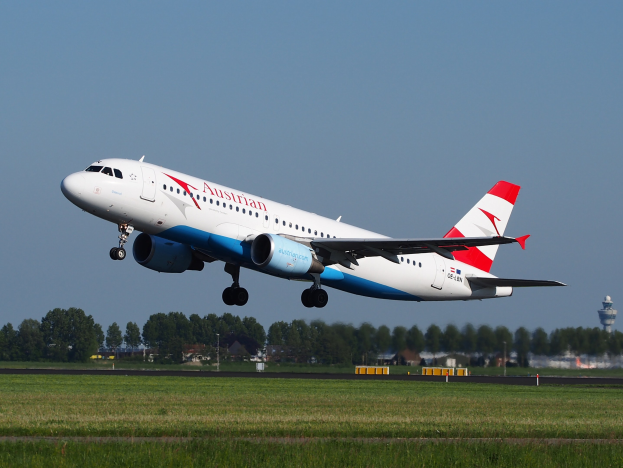 Airbus A320-200 der Austrian Airlines startet vom Frankfurter Flughafen mit grünem Gras darunter, Bäumen und Gebäuden im Hintergrund und einer Kontrollturm auf der rechten Seite.