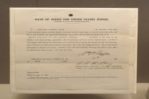 Papier mit gedrucktem Text, betitelt "Eidurkunde für US-Richter" auf einem Tisch vor einer Wand.