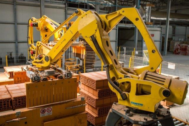 Großes industrielles Lager mit gestapelten Kisten, Kränen an der Decke, Zaun, Pfosten und einer fernen Wand in einer automatisierten Fertigungsumgebung.