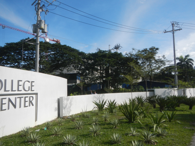 Eingang zu einem College-Zentrum mit einem "College-Zentrum"-Schild, umgeben von Grün, einem Weg, Strommasten, Gebäuden, einem Kran und einem bewölkten Himmel.
