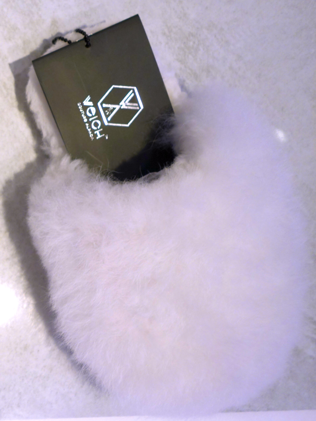 Ein weißer Pelzbeutel mit einer schwarzen Markierung, aus Schafsfell hergestellt, auf einer weißen Oberfläche.