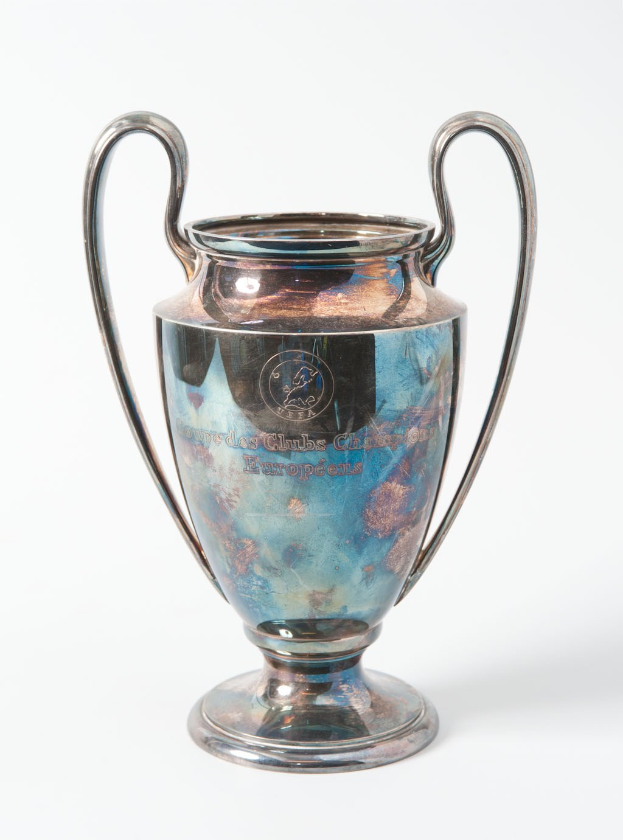 Der UEFA Champions League Pokal, ein stahlerner Becher mit zwei Griffen und einem blauen und silbernen Farbschema, beschriftet mit «UEFA Champions League», gegen einen weißen Hintergrund dargestellt.