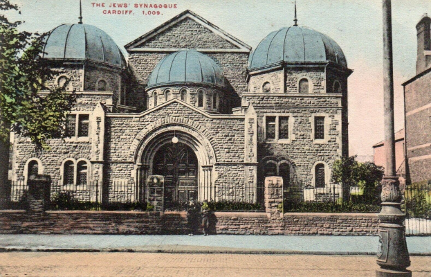 Alte Postkarte der jüdischen Synagoge in Cardiff, Ontario, Kanada, die ein Gebäude mit Fenstern, Türen und Bögen zeigt, umgeben von Pflanzen, einem Zaun, Bäumen, einem Pfahl und einem bewölkten Himmel, mit Text oben.